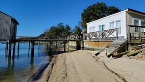 A beach with a wooden pier connecting to a white building with a balcony. - The Boat House - Water Front, Wifi, Pet Friendly 1 Bedroom Home by RedAwning (Norfolk)