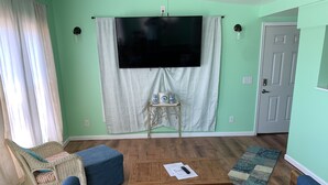 A living room with a large flat-screen TV, a sofa, a coffee table, and a wicker chair. - The Boat House - Water Front, Wifi, Pet Friendly 1 Bedroom Home by RedAwning (Norfolk)