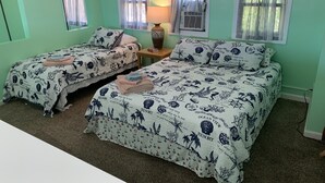 A room with two beds, each with matching ocean-themed bedding. There is a lamp on a nightstand between the beds, and a window with a curtain. - The Boat House - Water Front, Wifi, Pet Friendly 1 Bedroom Home by RedAwning (Norfolk)