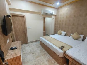 A bedroom with a bed, a desk, an air conditioning unit, and a mirror. - Hotel Sarnath International  (Varanasi)