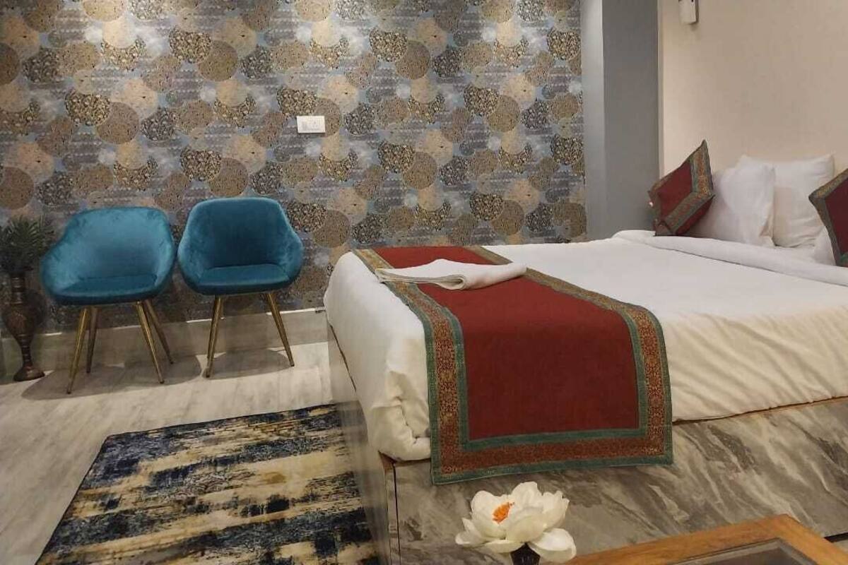 A hotel room with a bed, two blue chairs, a patterned wall, and a decorative rug.