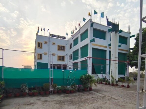 A multi-story hotel with a green and white facade, multiple flags, and a fenced outdoor area with potted plants. - Hotel Sarnath International  (Varanasi)