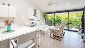 A modern living room with a white sofa, a dining table, and a balcony with a view of greenery. - Private Rooftop Terrace + Walkable to the Beach (Bays of Huatulco)