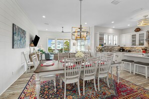 Une cuisine moderne avec des meubles blancs, un coin repas doté d’une table en bois et de chaises blanches, et un tapis aux couleurs vives.