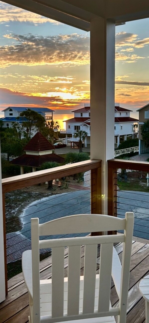 A balcony with a white chair, overlooking a residential area with houses and a sunset view.