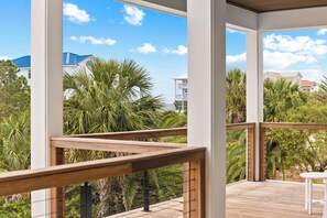 A wooden deck with a white railing, overlooking a lush garden and buildings with blue roofs.