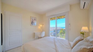 Ein Schlafzimmer mit einem großen Bett, einem Sessel, einem Gemälde, einem Balkon mit Aussicht und einer Klimaanlage.