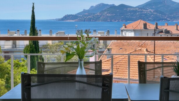 Ein Balkon mit Blick auf das Meer und die Berge, eine Vase mit Blumen und ein Tisch mit Stühlen.