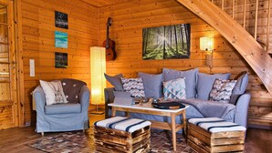 Un accogliente interno di una baita con arredamento in legno, un divano, una poltrona, un tavolo e una chitarra.