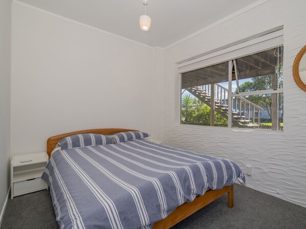 Un dormitorio con cama, ventana y pared blanca con textura.