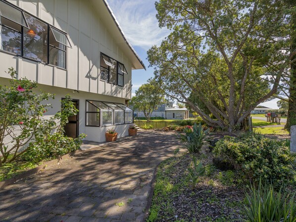 A two-story building with large windows, a covered patio area, and a garden with various plants and a tree.