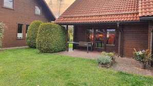 Een houten huis met pannendak, een overdekt terras en een verzorgd gazon.