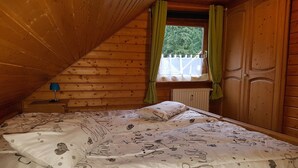 Een gezellig zolderkamer met schuine wanden, een enkel bed met beddengoed met een patroon, een nachtkastje met een lamp en een raam met gordijnen.