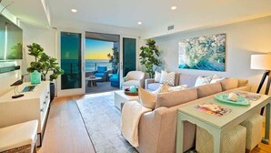A modern living room with a sofa, a coffee table, and a TV. There is a sliding glass door leading to a balcony with a view of the ocean. - Stunning Oceanfront Getaway at Windansea Beach (San Diego)