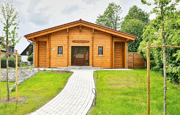 A wooden cabin with a paved entrance, surrounded by greenery and trees.