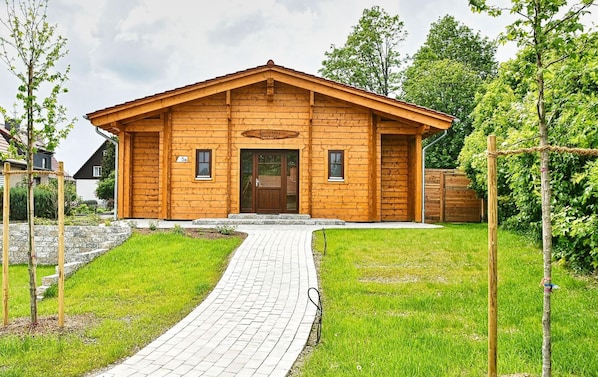 A wooden cabin with a paved entrance, surrounded by greenery and trees.