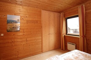 Una habitación con paneles de madera, una cama, una ventana con cortinas y un cuadro en la pared.