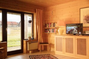 A cozy room with a wooden interior, a radiator, a bookshelf, a television, and a window with curtains. - Doppelhaushälfte in Hasselfelde (Hasselfelde)