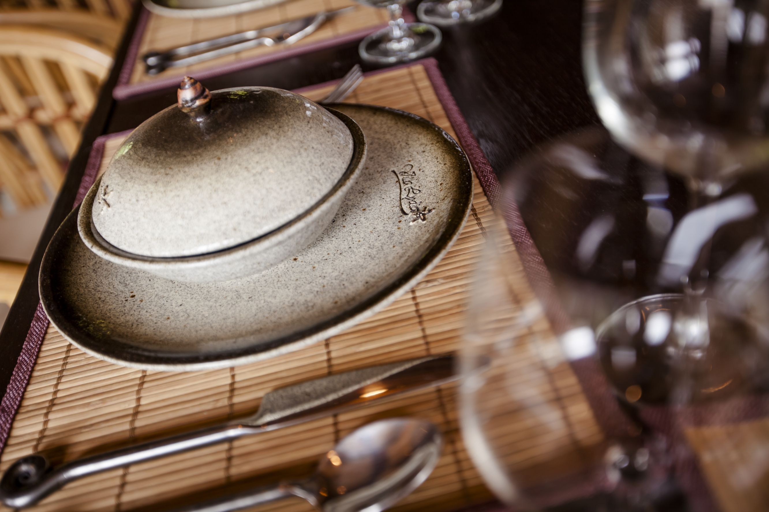 A dining table with a ceramic pot, a plate, and cutlery.