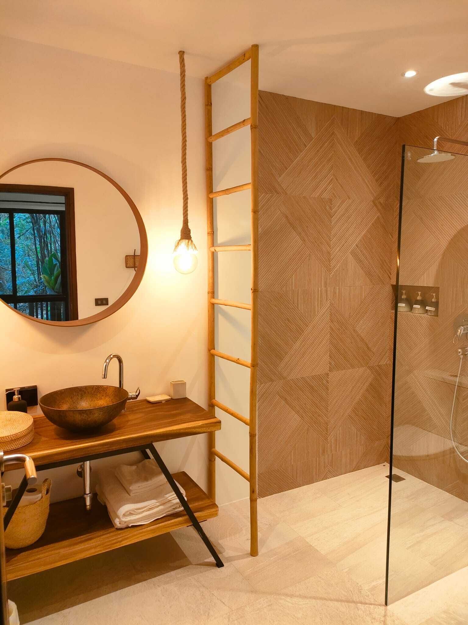 A modern bathroom with a round mirror, wooden vanity, and a glass shower enclosure.