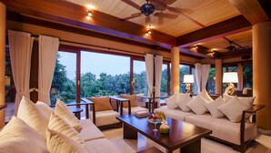 A spacious room with a large window, a ceiling fan, and a table with a bowl of fruit and a drink. - Villa Lydia, Koh Yao Noi (Ko Yao)