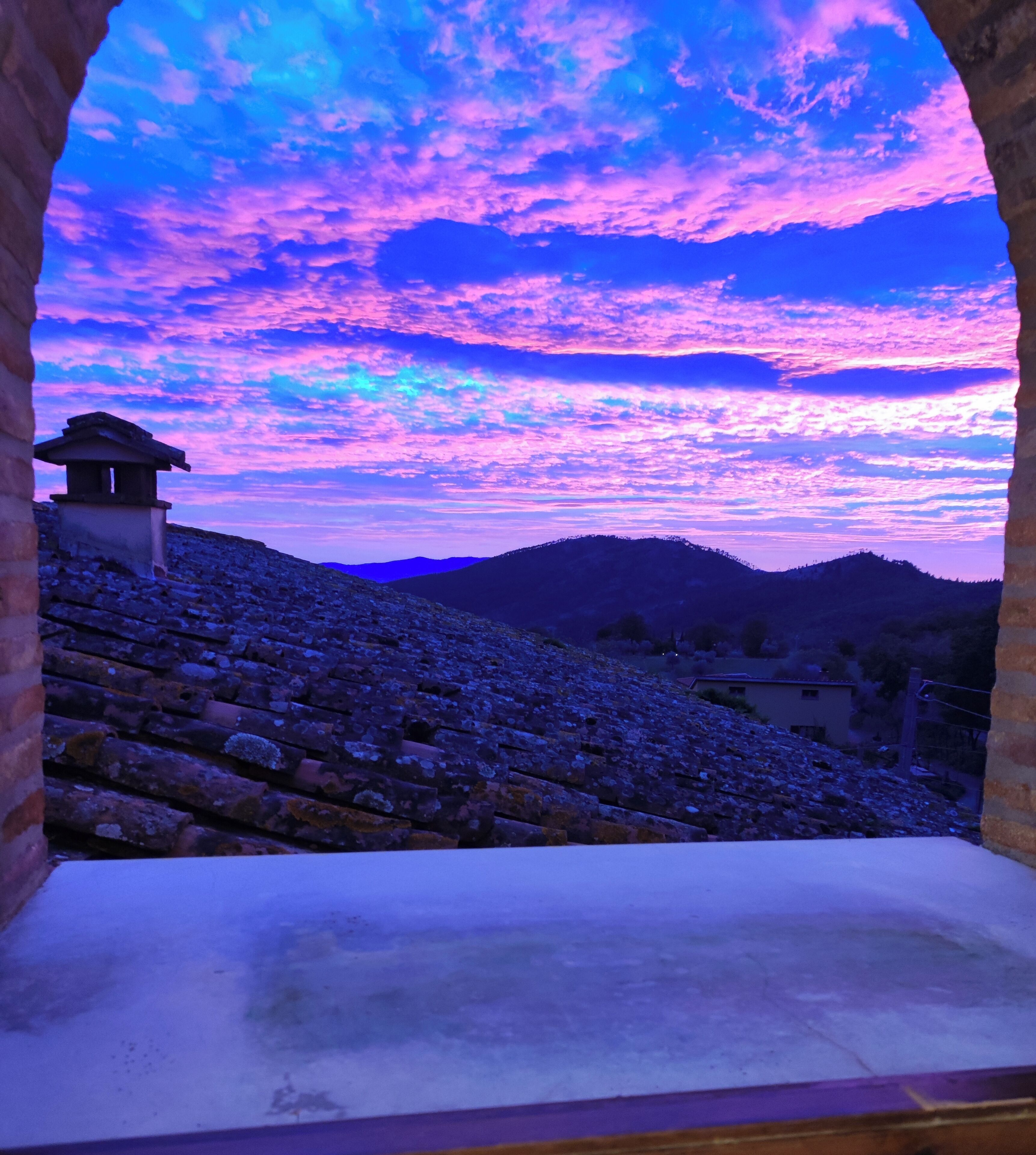 A stone structure with a traditional roof, set against a backdrop of a mountainous landscape and a vibrant sky.