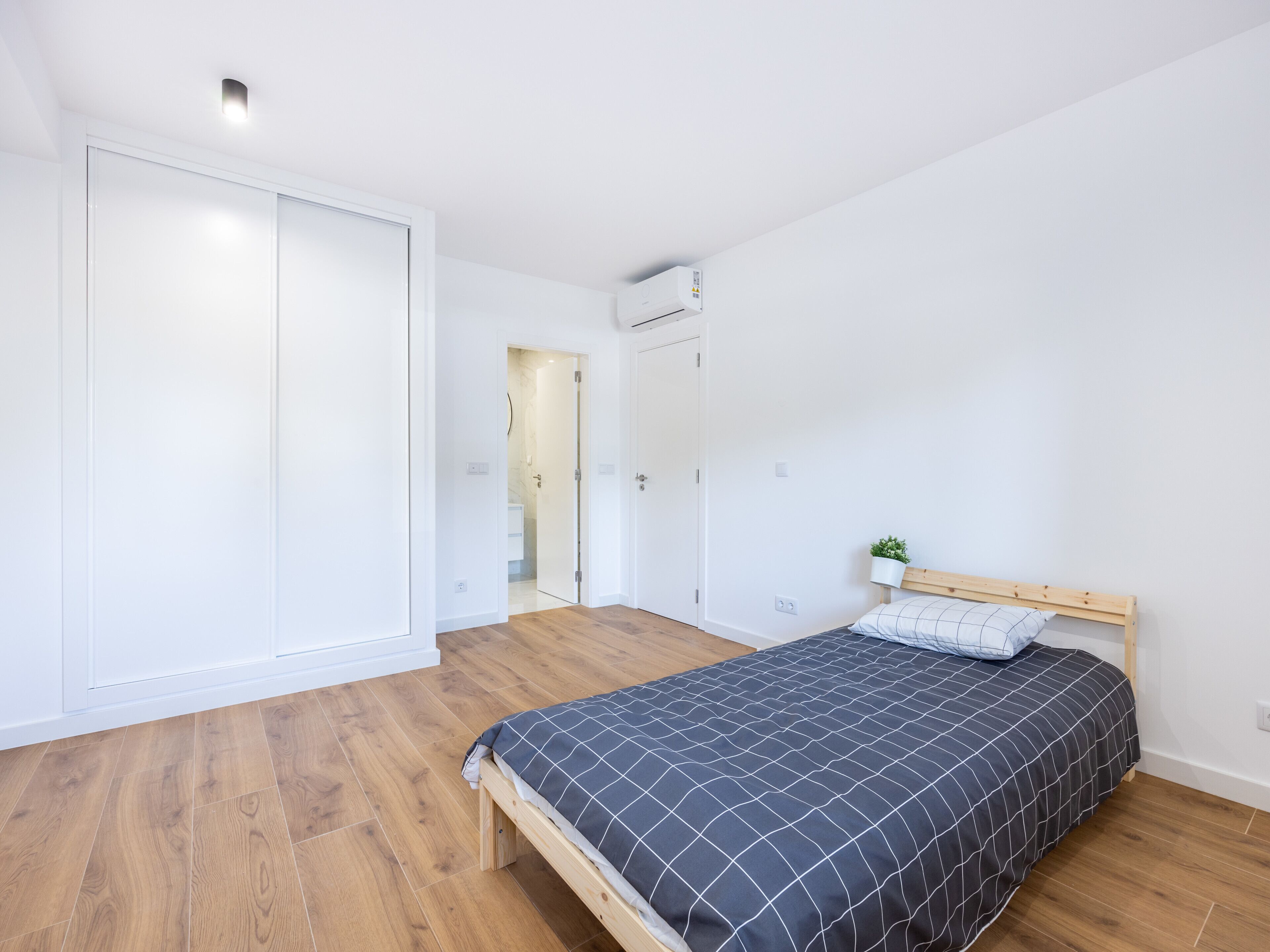 A bedroom with a wooden floor, a bed with a black and white checkered bedspread, a wooden headboard, and a white wardrobe.