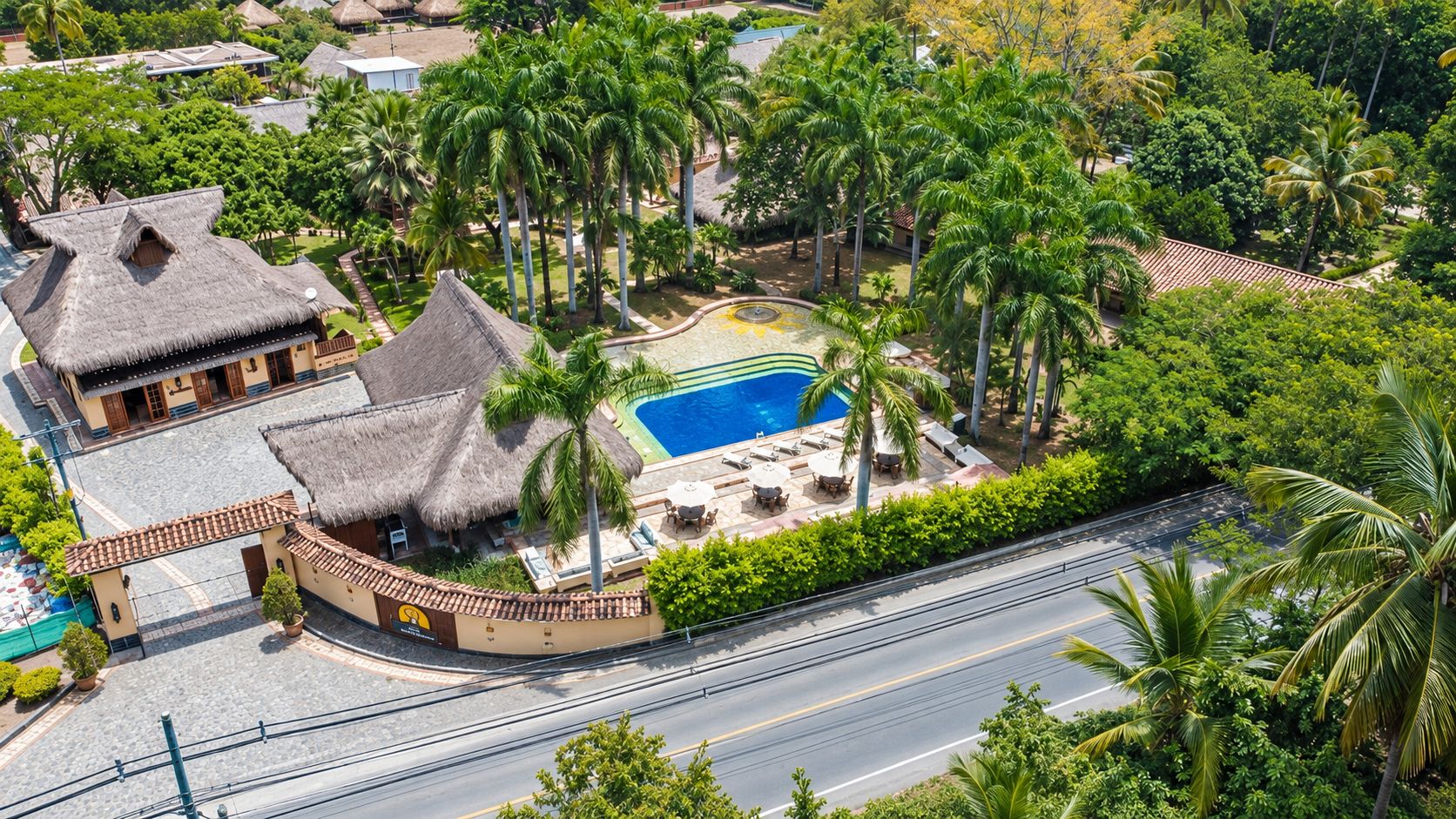 Un complejo turístico con piscina, palmeras y edificios de techo de paja.