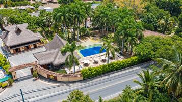 Un complejo turístico con piscina, palmeras y edificios de techo de paja.