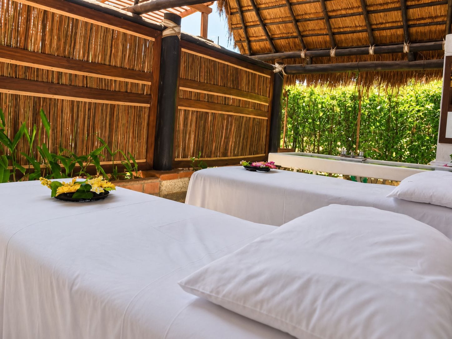 A room with two beds, a thatched roof, and a bamboo wall.