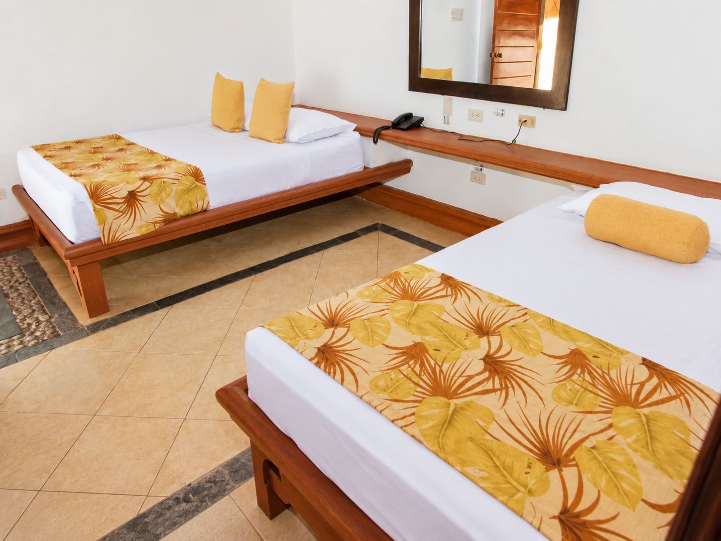 Une chambre d’hôtel avec deux lits simples, un banc en bois, un téléphone et un miroir au mur.