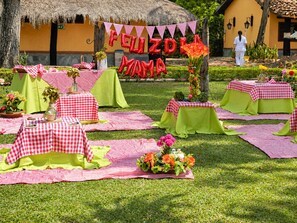 An outdoor dining area with checkered tablecloths, floral centerpieces, and a banner reading 'Feliz Dia Mama.' - Hotel Porton del Sol  (Santa Fe de Antioquia)