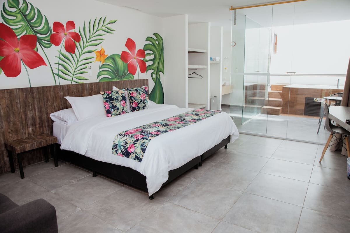 A bedroom with a bed, a wooden bench, a tropical mural, and a view of a balcony.