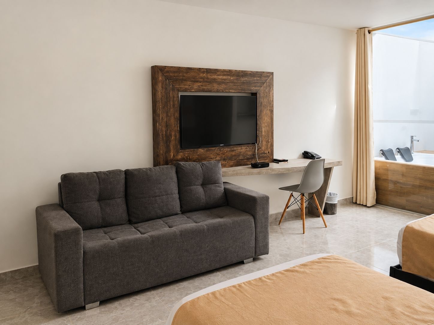 Habitación de hotel moderna con un sofá gris, un escritorio, un televisor y un ventanal grande.