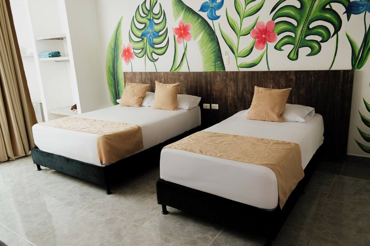 A hotel room with two beds, beige bedding, and a wall mural of tropical leaves and flowers.