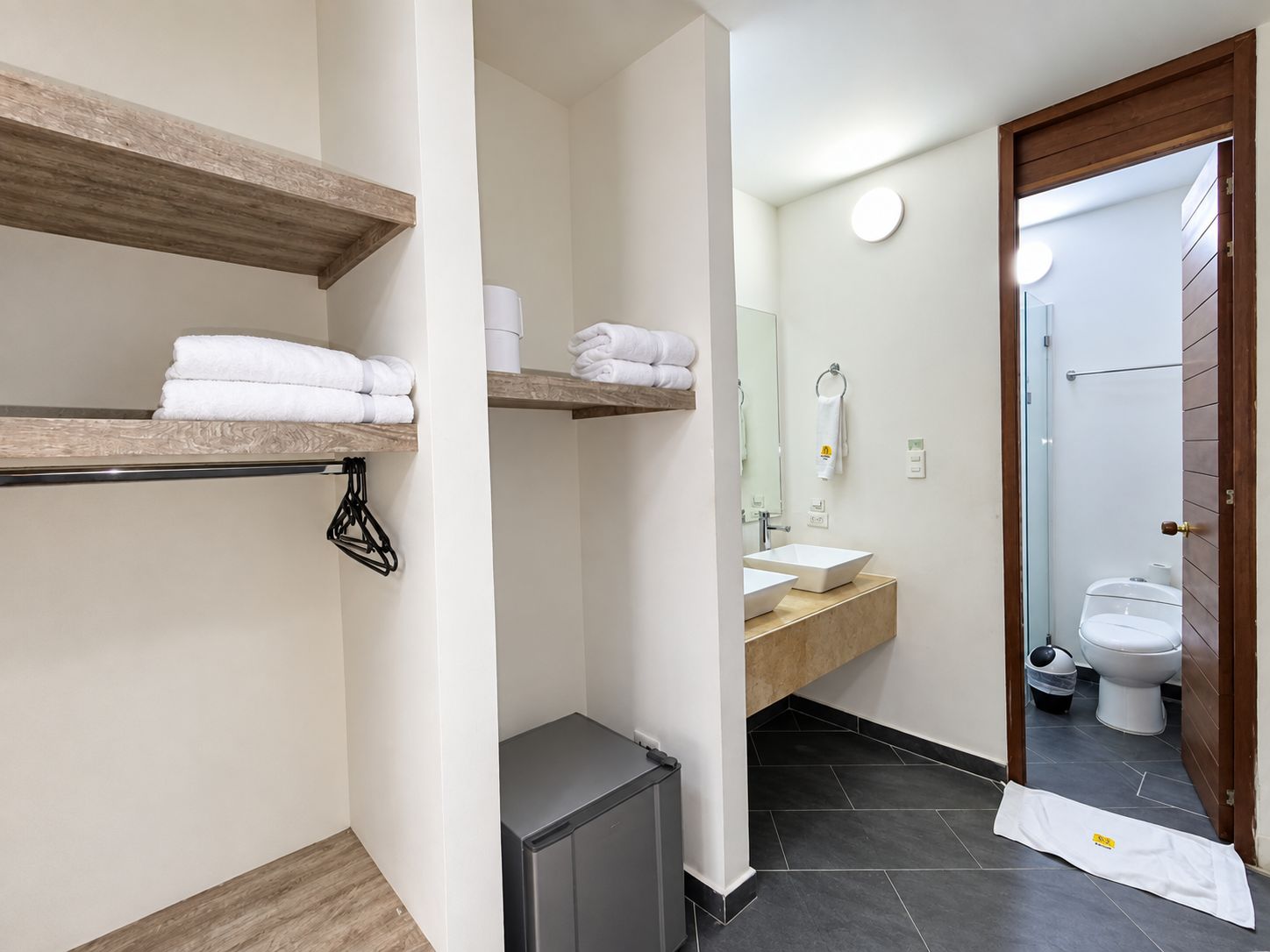 Un baño con estante de madera con toallas, un lavamanos con espejo y un inodoro.