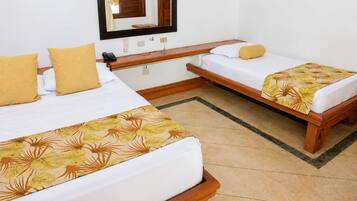 Quarto de hotel com duas camas de solteiro, um banco de madeira, uma mesinha, um espelho e um edredom com padrão floral.
