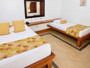 Habitación de hotel con dos camas individuales, un banco de madera, una mesita, un espejo y una colcha con estampado floral.
