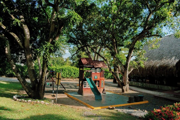 A playground with a slide, swings, and a small building with a thatched roof. - Hotel Porton del Sol  (Santa Fe de Antioquia)