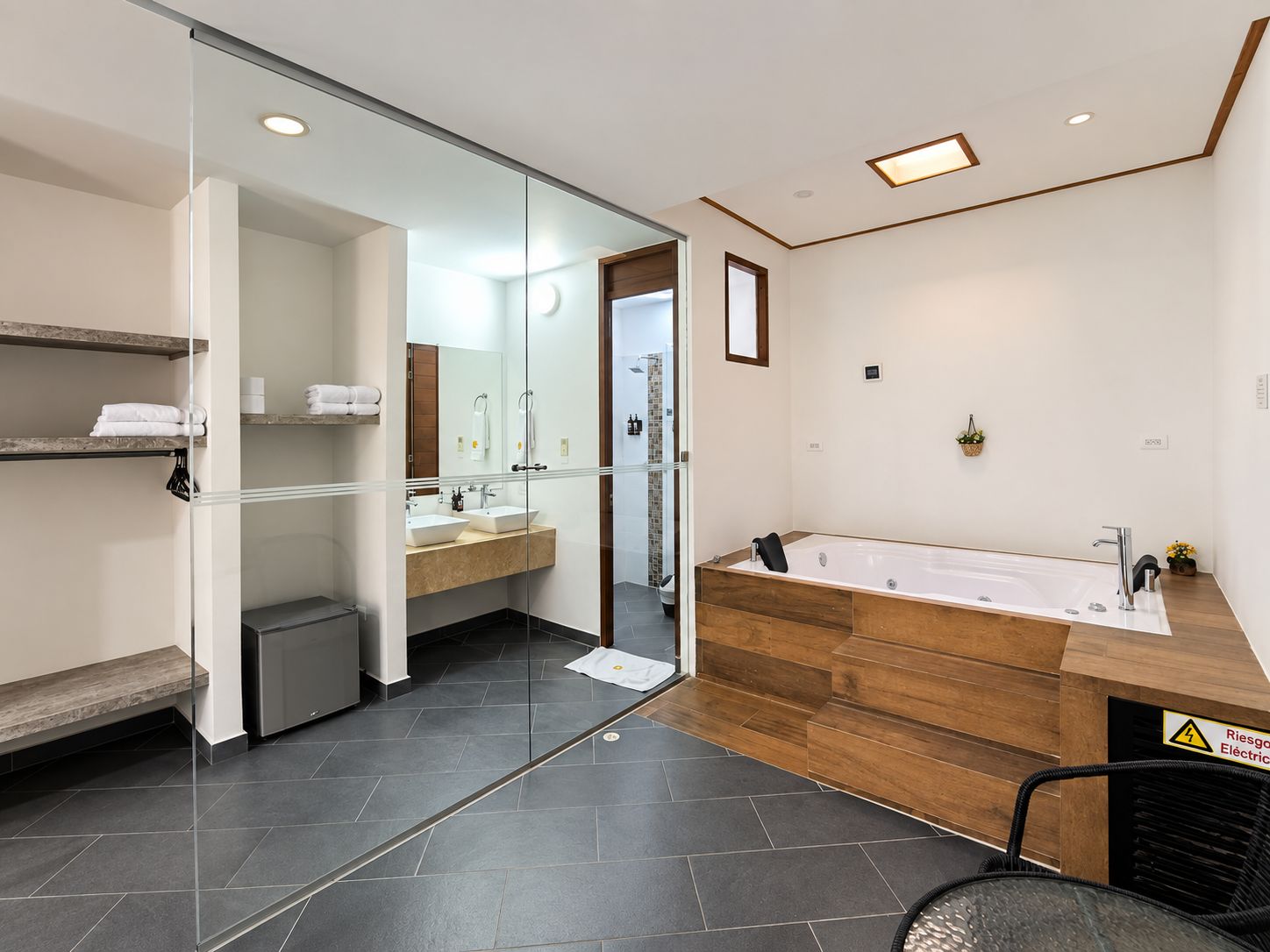 A modern bathroom with a large bathtub, two sinks, a glass shower enclosure, and a bench.