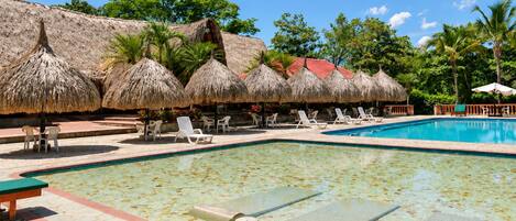 A pool area with lounge chairs and thatched umbrellas.