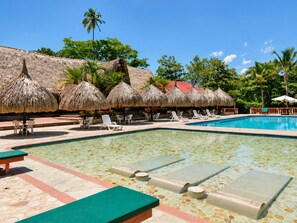 Un área de piscina con sillones de descanso y sombrillas de techo de paja.