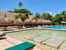 Un área de piscina con sillones de descanso y sombrillas de techo de paja.