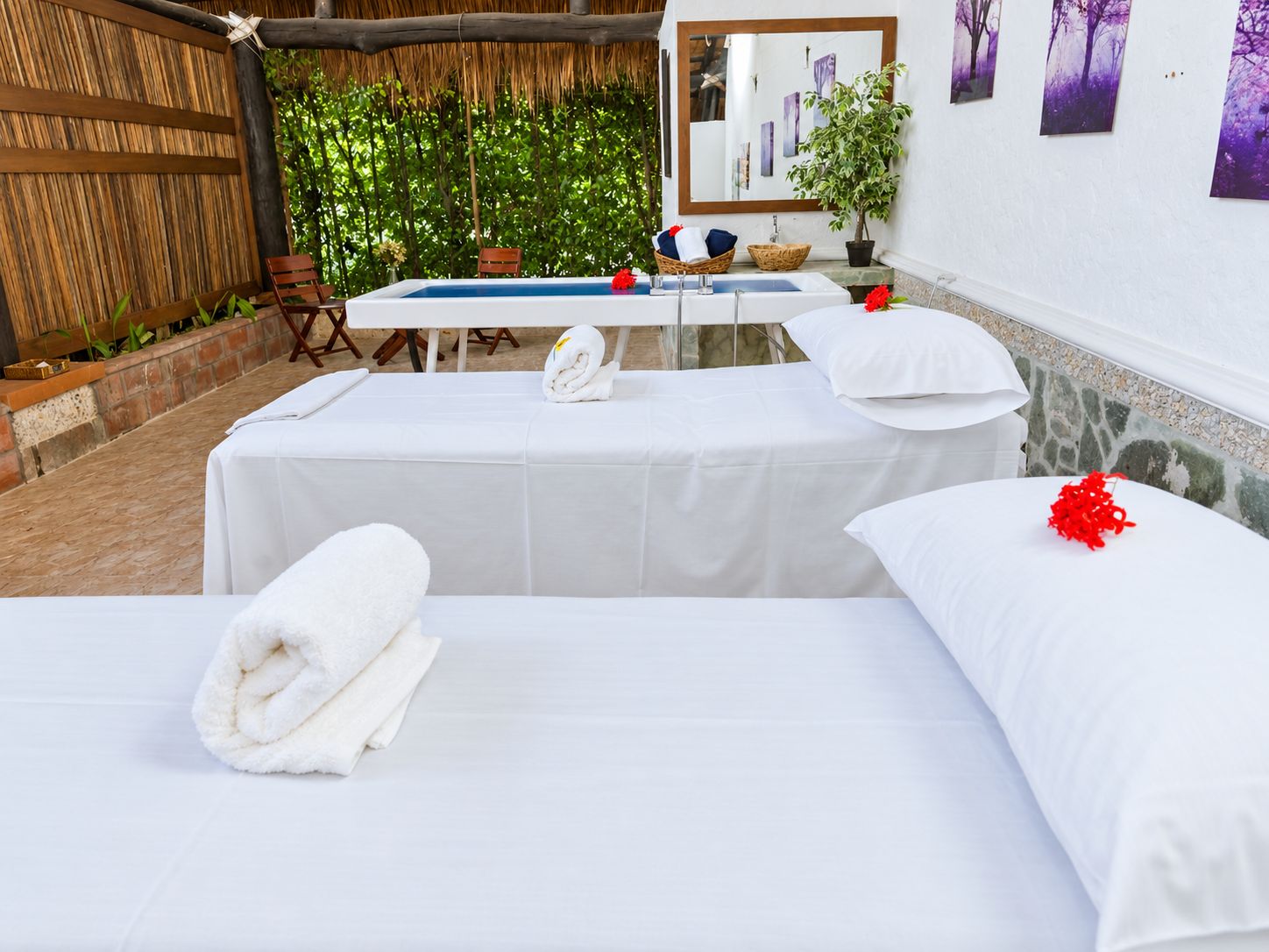A spa room with two beds, a massage table, a small pool, and a wooden fence.