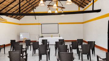 Un salón de conferencias con una pizarra, pantalla de proyector y sillas de mimbre dispuestas en filas.
