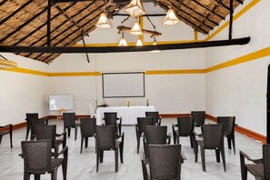 Un salón de conferencias con una pizarra, pantalla de proyector y sillas de mimbre dispuestas en filas.