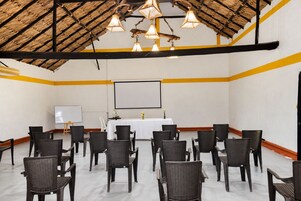 Un salón de conferencias con una pizarra, pantalla de proyector y sillas de mimbre dispuestas en filas.