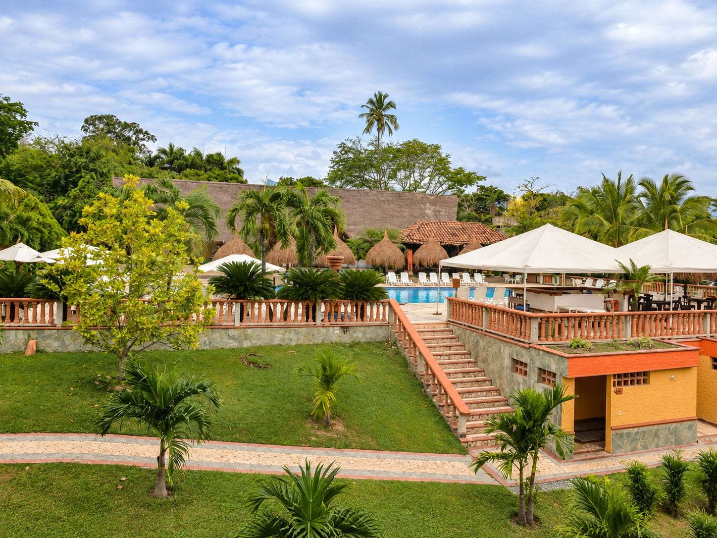 A resort with a swimming pool, outdoor seating, and a staircase leading to a building.