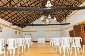 Un salón de conferencias con sillas blancas dispuestas en filas, una pizarra y un techo de madera con luces colgantes.