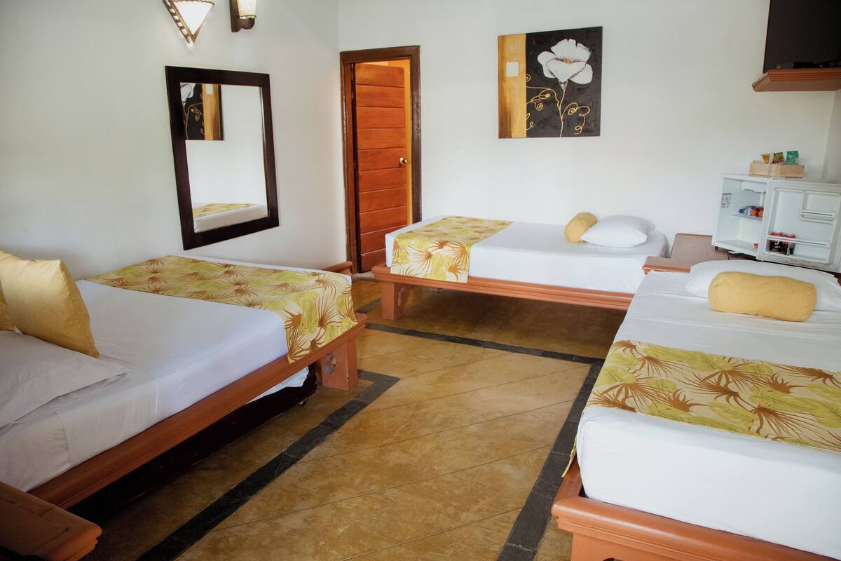 A hotel room with two single beds, a wooden wardrobe, a mirror, and a wall-mounted TV.